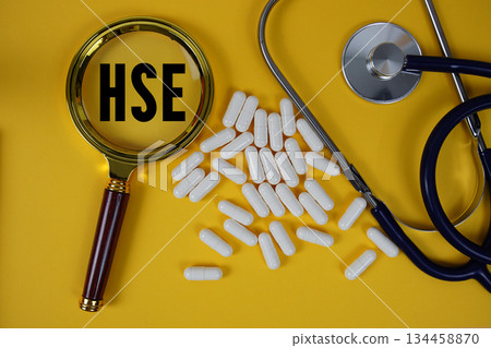 HSE Health Safety Environment text with magnifying glass and Stethoscope on yellow background 134458870