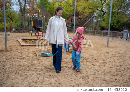 Mother and daughter holding hands and walking together in a sandy playground. Quality time and peaceful moments in autumn. 134458910