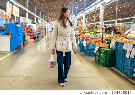 Woman walking through indoor farmers market with a bag of groceries. Urban weekend food shopping. 134458915