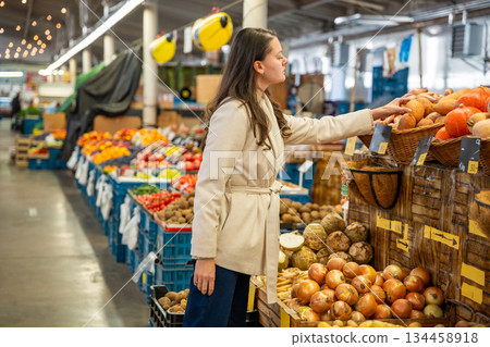 Woman shopping for fresh produce at a local indoor market. Choosing healthy vegetables and fruit during grocery run. 134458918