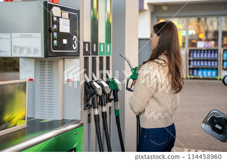 Back view of woman preparing to pump fuel into her car. Routine car maintenance at gas station. Back view of woman preparing to pump fuel into her car. Routine car maintenance at gas station. 134458960