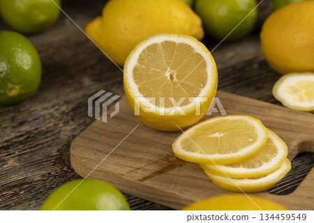 sliced yellow sour lemon lying on the table with green limes, sliced ripe citrus fruits lemon and limes are lying on a wooden table 134459549