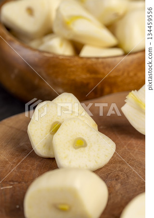 peeled and sliced purple garlic scattered on the black kitchen table and peeled and sliced fragrant fresh garlic spices scattered on the kitchen table during cooking 134459556