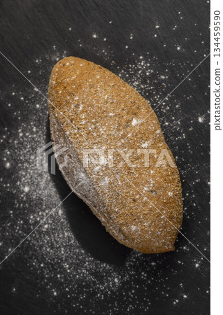 a fresh soft loaf of bread on black slate, a fresh soft loaf of rye bread lies on the table a fresh soft loaf of bread on black slate, a fresh soft loaf of rye bread lies on the table 134459590