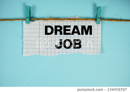 Dream Job text written on rip paper with wooden clip on blue background Dream Job text written on rip paper with wooden clip on blue background 134459707