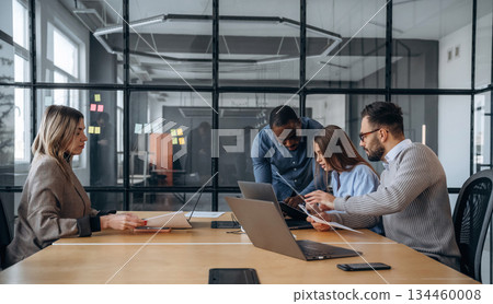 Calm, sitting by the table. Professional workers are in the modern office together Calm, sitting by the table. Professional workers are in the modern office together 134460008