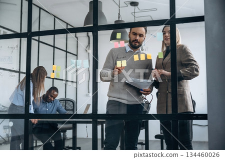 Bunch of stickers on the glass. Professional workers are in the modern office together Bunch of stickers on the glass. Professional workers are in the modern office together 134460026