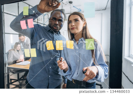 Paper stickers on the glass. Professional workers are in the modern office together 134460033