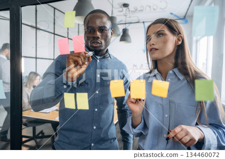 Paper stickers on the glass. Professional workers are in the modern office together Paper stickers on the glass. Professional workers are in the modern office together 134460072