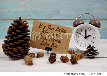 It's The Little Moments That Make Life Big text written on paper card with alarm clock and pine cones decoration on wooden background 134460935