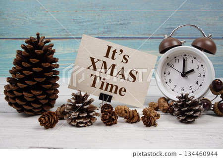 It's XMAS Time text written on paper card with alarm clock and pine cones decoration on wooden background 134460944