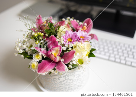 Elegant bouquet of pink orchids and daisies on white desk. Balance of work, beauty, and peaceful home ambiance. 134461501