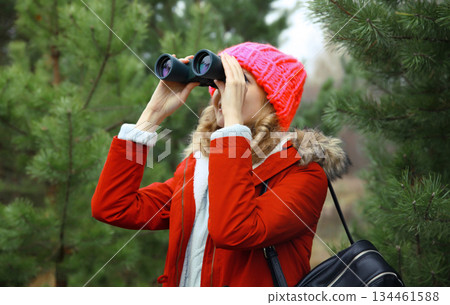 Woman tourist looking through binoculars watching nature, wild animals walking in winter forest Woman tourist looking through binoculars watching nature, wild animals walking in winter forest 134461588