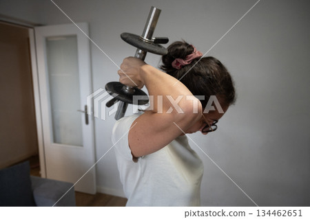 Woman doing triceps exercise with dumbbell at home 134462651