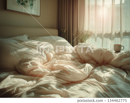 Morning light fills cozy bedroom with rumpled bed and warm cup of coffee on the side table 134462775