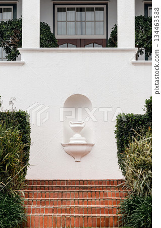 Classic white stucco facade with red brick stairs and lush green bushes 134463588