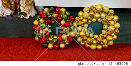 Two Christmas bauble wreaths in red green and gold placed on festive carpet. Holiday showroom atmosphere, winter decoration tradition and cheerful seasonal celebration mood 134463606