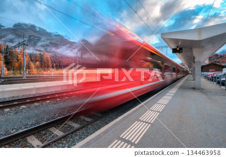 Blurred red passenger train passing mountain railway station Blurred red passenger train passing mountain railway station 134463958