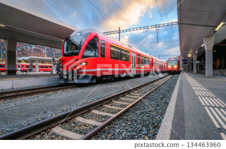 Red modern passenger train on mountain railway station in Alps Red modern passenger train on mountain railway station in Alps 134463960