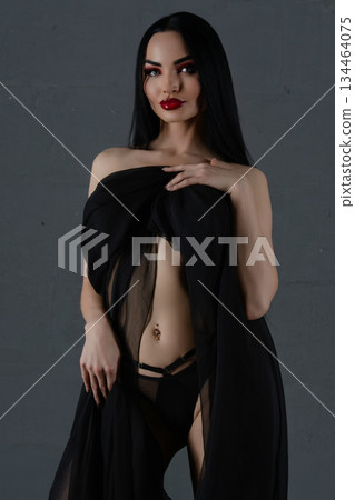 Elegant woman in black lingerie with flowing sheer fabric posing gracefully 134464075