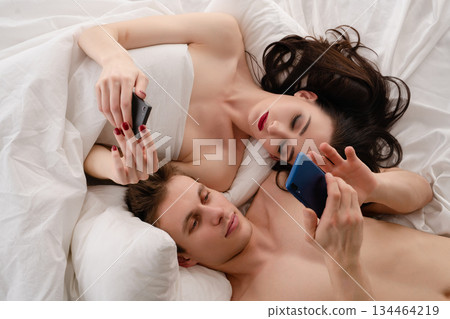 Couple enjoying intimate time together while using their smartphones in bed Couple enjoying intimate time together while using their smartphones in bed 134464219