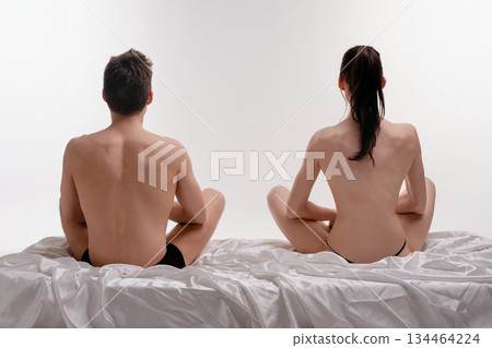 Couple sitting back to back on a bed, expressing intimacy in a cozy setting Couple sitting back to back on a bed, expressing intimacy in a cozy setting 134464224