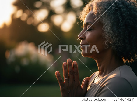 Peaceful senior black woman practicing mindfulness and meditation in warm evening light 134464427