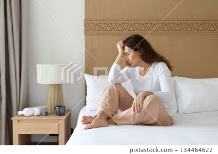 Thoughtful depressed woman sitting on bed in bedroom, resting head on hand 134464622