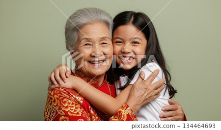 An elderly asian grandmother and her young granddaughter share a joyful hug with beaming smiles. An elderly asian grandmother and her young granddaughter share a joyful hug with beaming smiles. 134464693