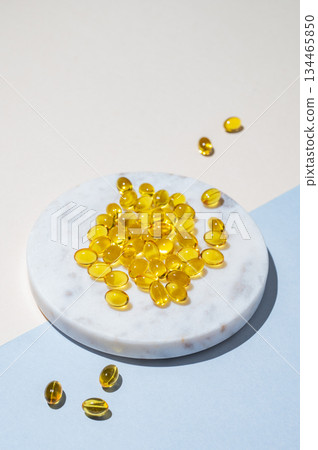 Yellow softgel vitamins capsules on a white marble plate on a blue background with shadow. Yellow softgel vitamins capsules on a white marble plate on a blue background with shadow. 134465850