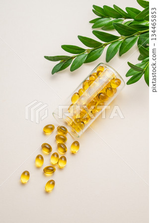 Yellow softgel vitamins capsules scattered in a bottle on a light background with green leaf. Yellow softgel vitamins capsules scattered in a bottle on a light background with green leaf. 134465853