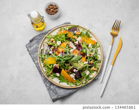 A fresh salad of beets, orange, and arugula with feta, walnuts, and balsamic dressing on a plate 134465861
