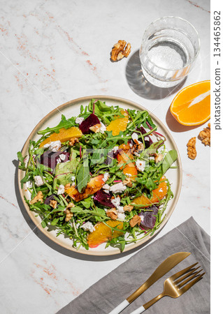 A fresh salad of beets, orange, and arugula with feta, walnuts, and balsamic dressing on a plate 134465862