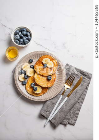 Pancakes with blueberry and banana on a marble background with cutlery, honey Pancakes with blueberry and banana on a marble background with cutlery, honey 134465869