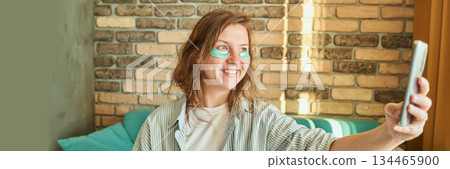 Caucasian young female enjoying morning skincare routine with eye patches while 134465900