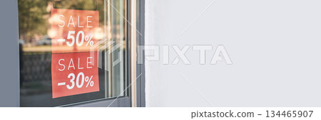 Storefront sale signs displaying 50 and 30 percent discounts on glass door 134465907