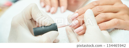 Close-up of manicure process with female hands and light pink nail polish Close-up of manicure process with female hands and light pink nail polish 134465942