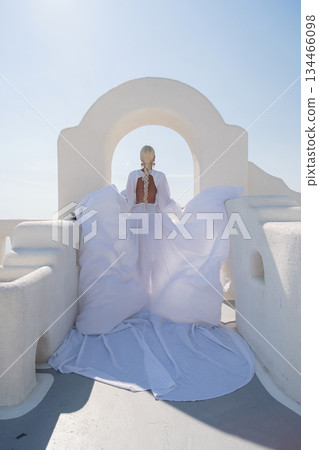 Wedding Santorini Dress: Bride stands in Santorini, Greece on a sunny day wearing flowing white gown. 134466098