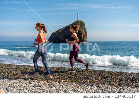 Running fitness women training actively on sunny pebble beach coastline 134466117