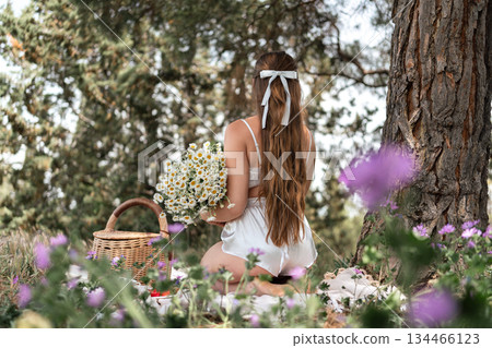 Picnic Flowers Woman: Back view girl with daisies at meadow picnic by tree enjoying summer day. Picnic Flowers Woman: Back view girl with daisies at meadow picnic by tree enjoying summer day. 134466123