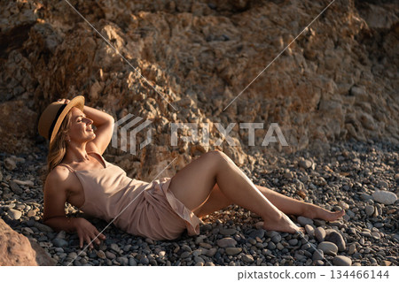 Woman, beach, relaxation, happy woman lying on a pebble beach, enjoying the warm summer sun on a peaceful vacation 134466144