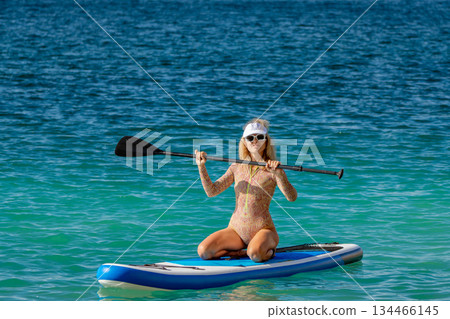 Woman, paddleboard, ocean, active young woman kneeling on a paddleboard in turquoise water with copy space 134466145