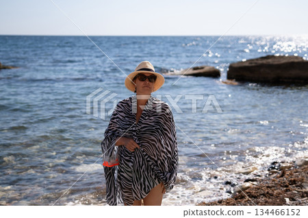 Woman beach summer A woman stands by the sparkling blue sea, wearing a hat and holding a snorkel mask, enjoying her sunny vacation. Woman beach summer A woman stands by the sparkling blue sea, wearing a hat and holding a snorkel mask, enjoying her sunny vacation. 134466152