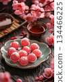 A plate of pink mochi sweets surrounded by cherry blossom flowers and a cup of tea. The scene is vibrant and inviting, showcasing traditional Asian desserts 134466225