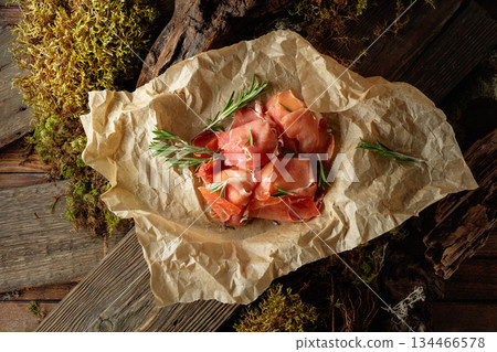 Prosciutto slices with rosemary wrapped in paper. 134466578