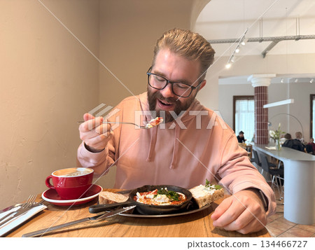 Man tasting breakfast in cafe. Connection between comfort, flavor and emotion through food, coffee and quiet morning atmosphere. Man tasting breakfast in cafe. Connection between comfort, flavor and emotion through food, coffee and quiet morning atmosphere. 134466727