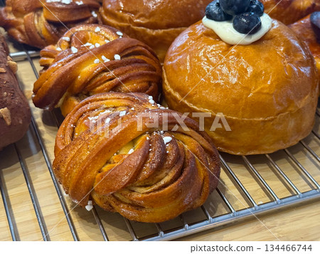 Round buns with cream and blueberries placed between almond croissants and pistachio rolls close-up. Bakery assortment symbolizing flavor, color, and craftsmanship. 134466744