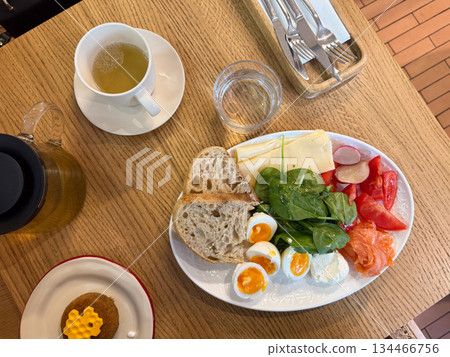 Morning meal with tea, honey dessert, eggs, vegetables, cheese, and bread arranged on wooden surface top view. Balanced breakfast symbolizing comfort and slow living. Morning meal with tea, honey dessert, eggs, vegetables, cheese, and bread arranged on wooden surface top view. Balanced breakfast symbolizing comfort and slow living. 134466756