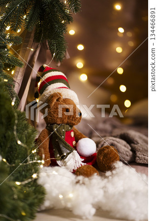 Plush bear in striped hat with snowball near Christmas tree lights 134466891