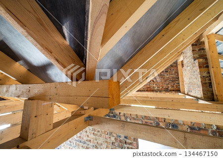 Attic of a building under construction with wooden beams of a roof structure and brick walls. Attic of a building under construction with wooden beams of a roof structure and brick walls. 134467150